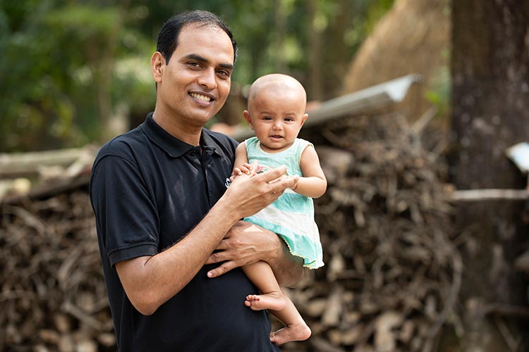 A man holding an infant in a mint green dress, smiling at the camera