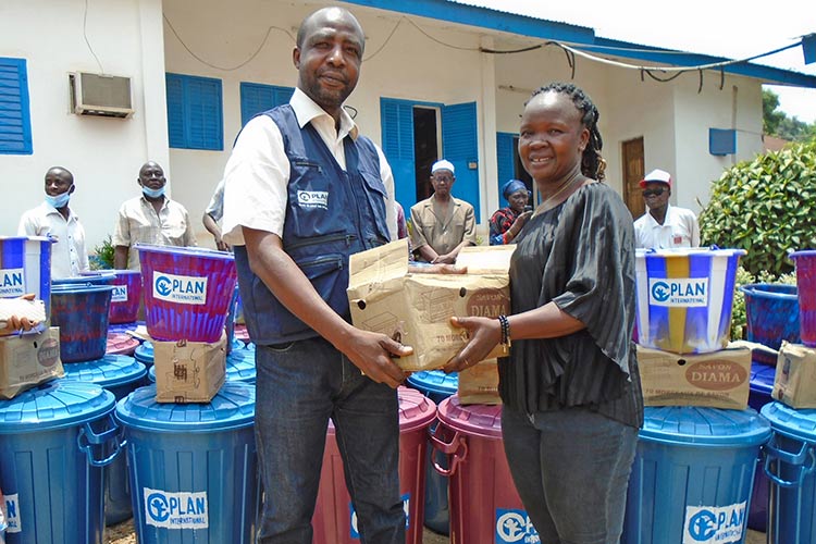 Plan Staff handing woman handwashing kit in Gueckedou 