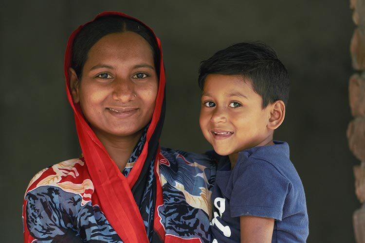 A smiling mother in blue and red shawl carrying her child