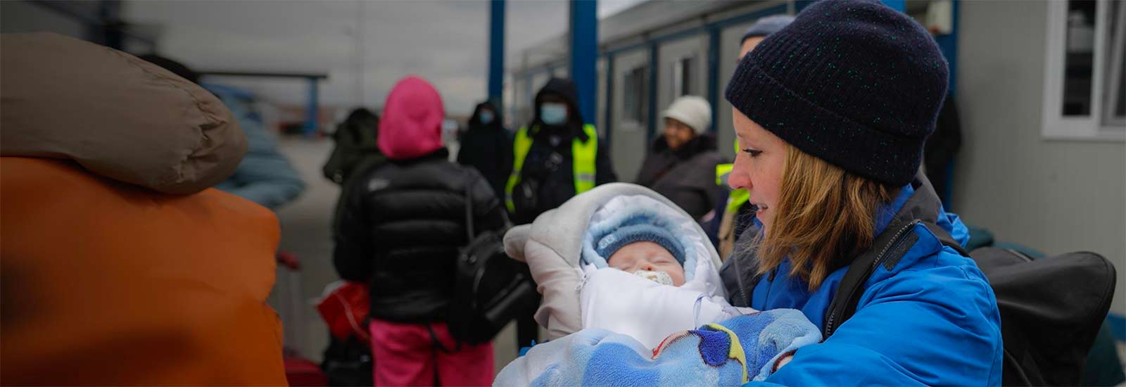 Katie Morrison, part of Plan International's response team, holds baby Daniil while family get paperwork ready to cross border