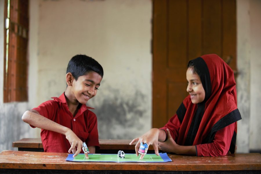 Two children smiling, playing the game of finger puppet together in a classroom