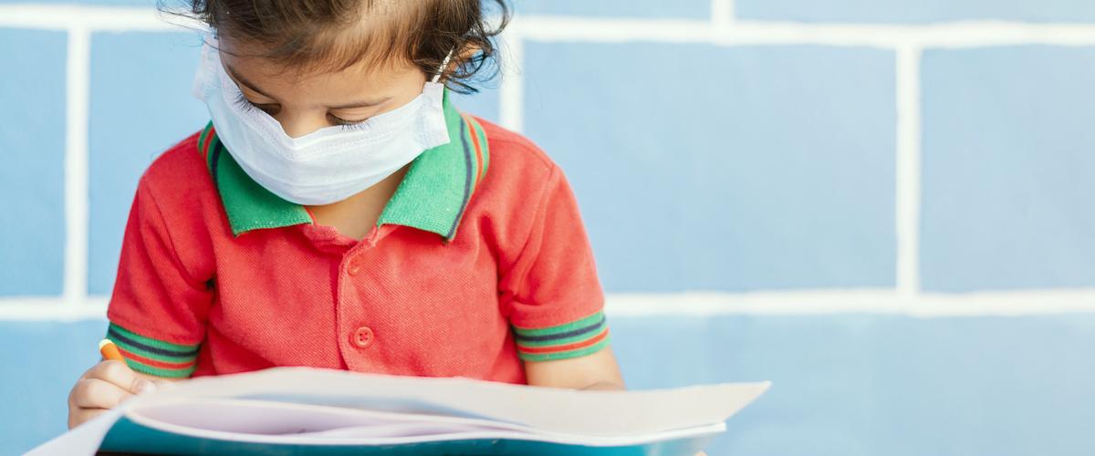 Young girl wears face mask while drawing picture