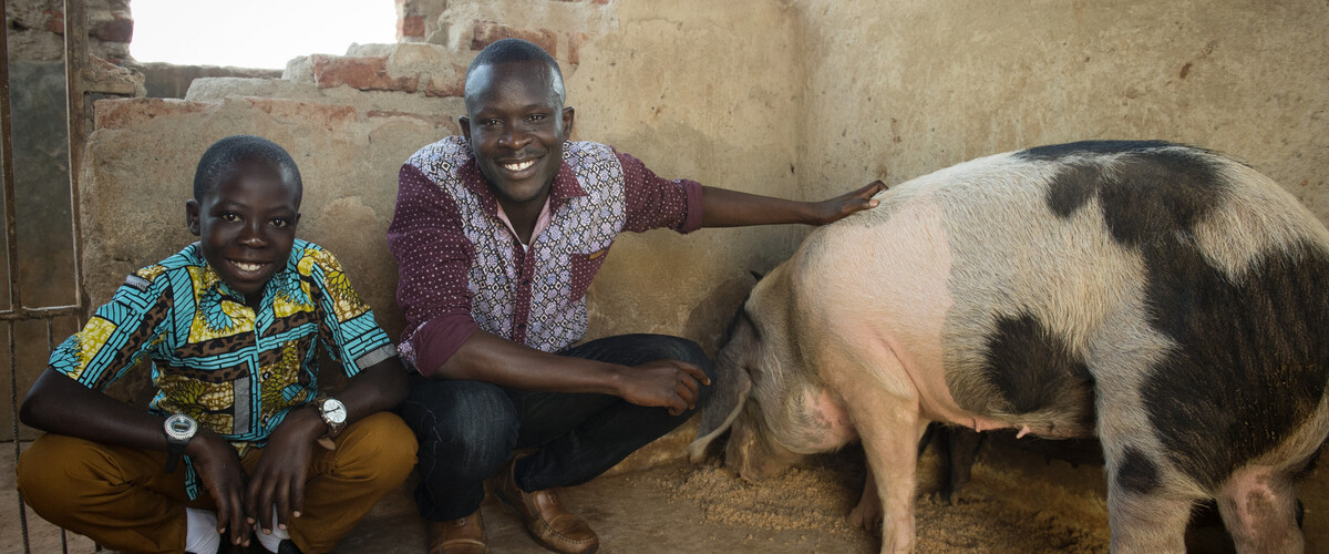 Ronald (centre) with his brother Alfred, 13 (left), inside his piggery in Uganda