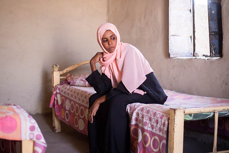  A woman wearing a shayla, sitting on a bed, looking to the side